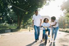 Man Standing Beside His Wife Teaching Their Child How to Ride Bicycle